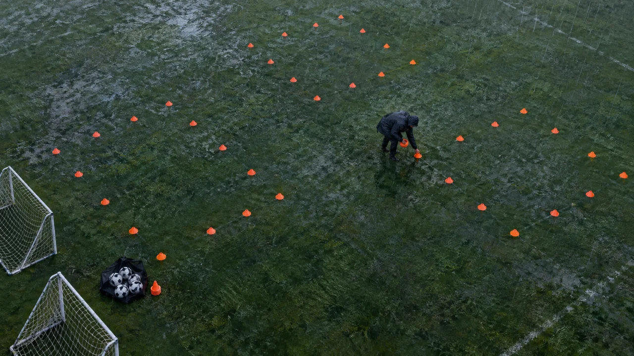Top-down view of a youth soccer coach setting up orange cone grids for a 9v9 practice on a wet, rainy field